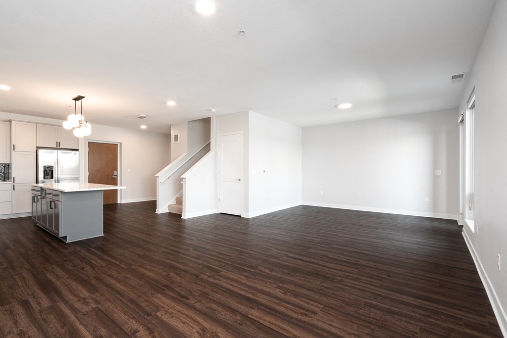 large open living and dining area with dark hardwood flooring. Kitchen counter and staircase to the left.
