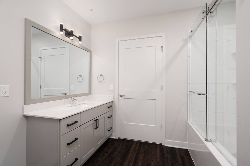 beautiful white bathroom with grey vanity and large mirror with glass shower doors