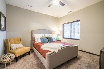 A bedroom with a bed, chair, and window.