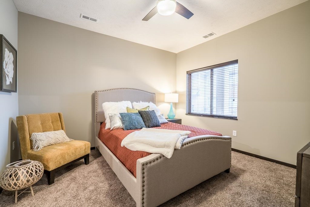 A bedroom with a bed, chair, and window.