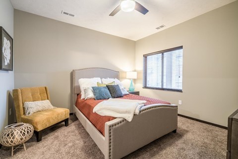 A bedroom with a bed, chair, and window.