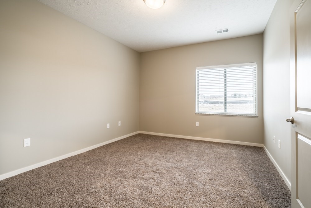 A bedroom with a carpeted floor and a window with blinds.