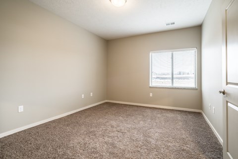 A bedroom with a carpeted floor and a window with blinds.