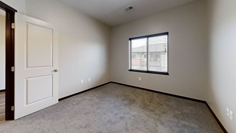 A room with a carpeted floor, a door, and a window with blinds.