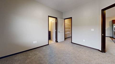 A room with a carpeted floor and a white wall with 2 doorways leading to bathroom and closet