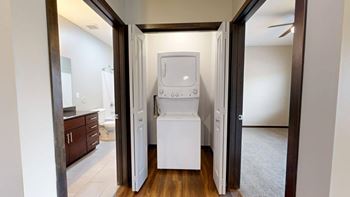 A white washing machine/dryer is in a closet between two rooms.