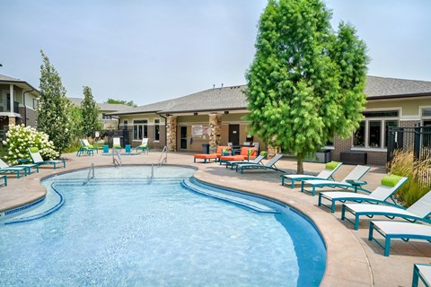 Organically shaped resort style pool surrounded a pool deck with bright blue lounge chairs