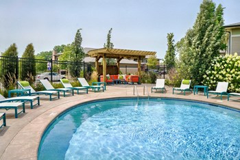 Edge of blue pool with lounge chairs around it and wood pergola in the background - Photo Gallery 9