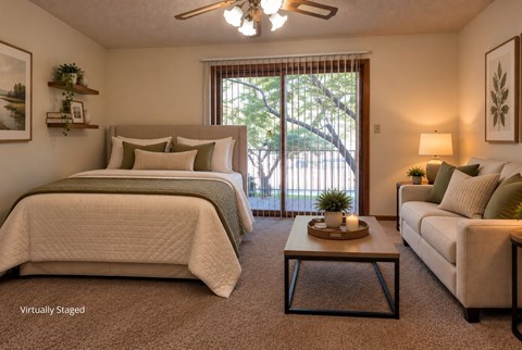 Virtually staged apartment bedroom with a seating area, carpet, ceiling fan, and sliding balcony doors.