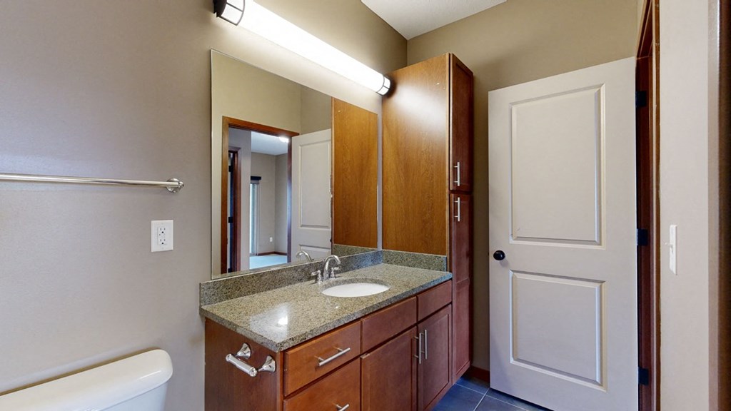 a bathroom with a granite sink vanity, a mirror, and overhead lighting