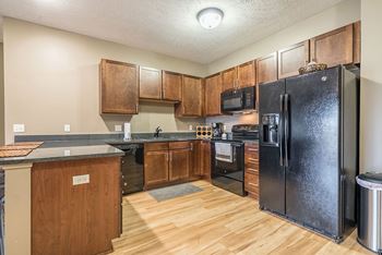 A kitchen with a black refrigerator and warm, medium brown wooden cabinets.