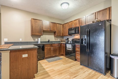 A kitchen with a black refrigerator and warm, medium brown wooden cabinets.