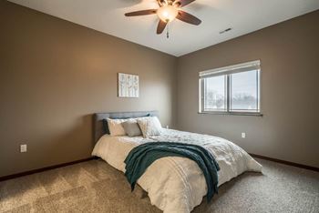 A bedroom with a bed, a ceiling fan, and a window.
