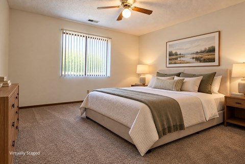 Virtually staged apartment bedroom with neutral finishes, a large window, carpeted flooring, and a ceiling fan.