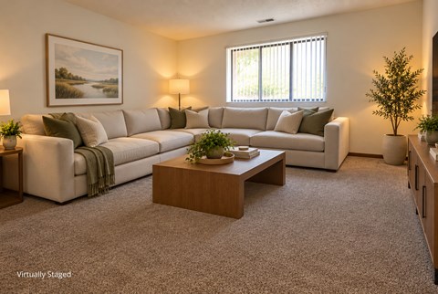 Virtually staged apartment living room with a large sectional sofa, warm neutral finishes, and natural light from a wide window.