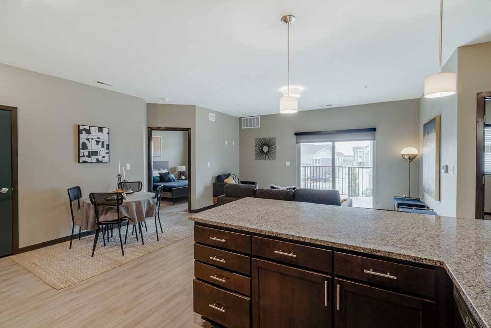 A kitchen with dark wood cabinets and a granite countertop in front of a living room