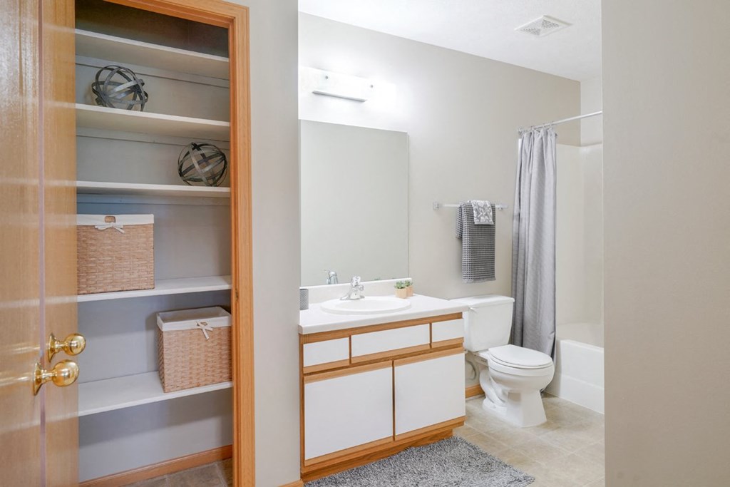 Linen closet next to bathroom with a toilet and a sink and a mirror and shower and tub combo