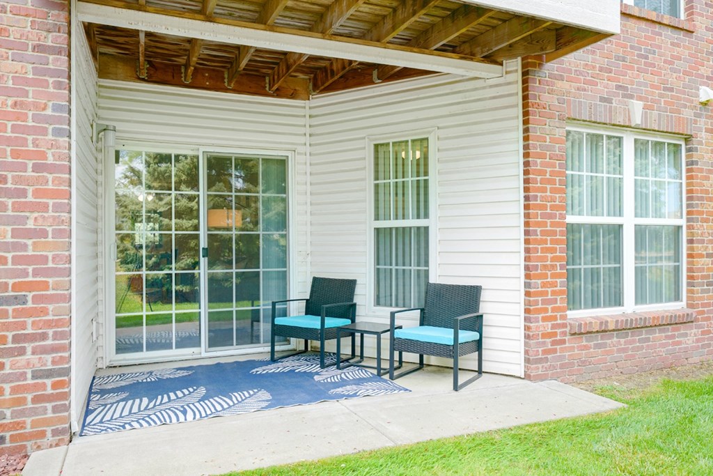 Back patio with two chairs and a rug in front of sliding glass door