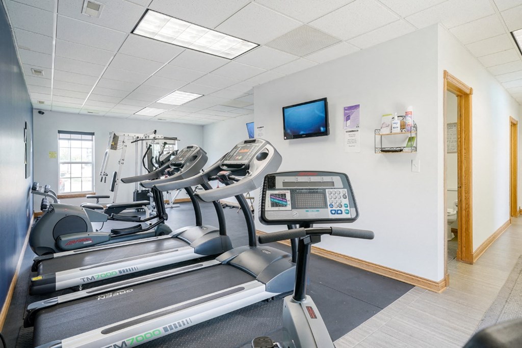 24-hour fitness center with a stationary bike, two treadmills, and an elliptical with a tv on the wall