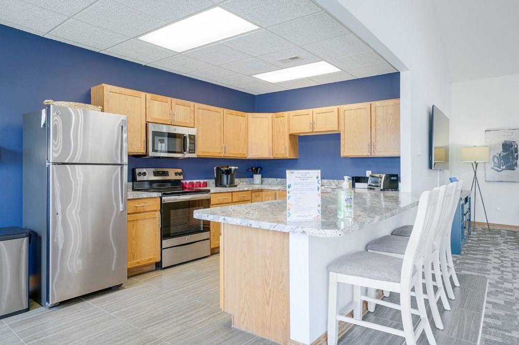Community kitchen with stainless steel appliances, blue accent wall, and a counter with chairs for dining