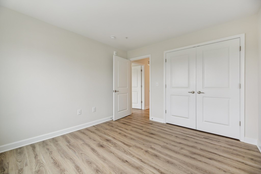 A room with white walls and wooden flooring, featuring a doorway and two white doors.