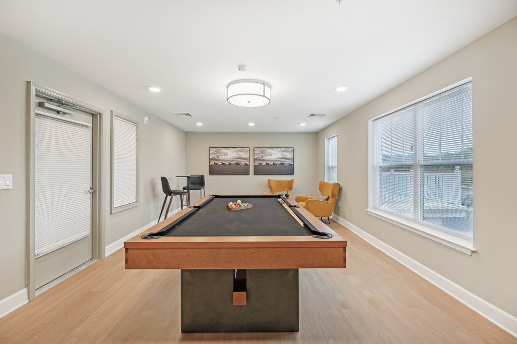 A pool table is in the middle of a room with a picture on the wall and a window with blinds.