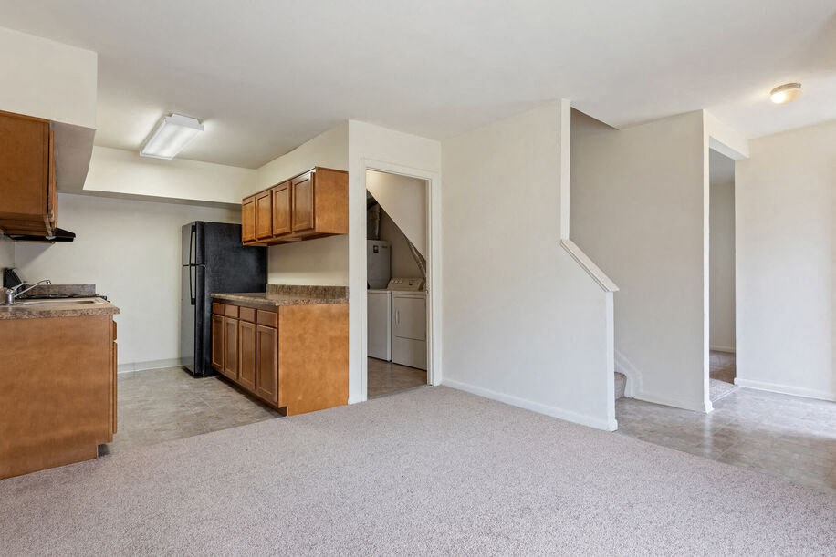an empty living room with a kitchen in the background