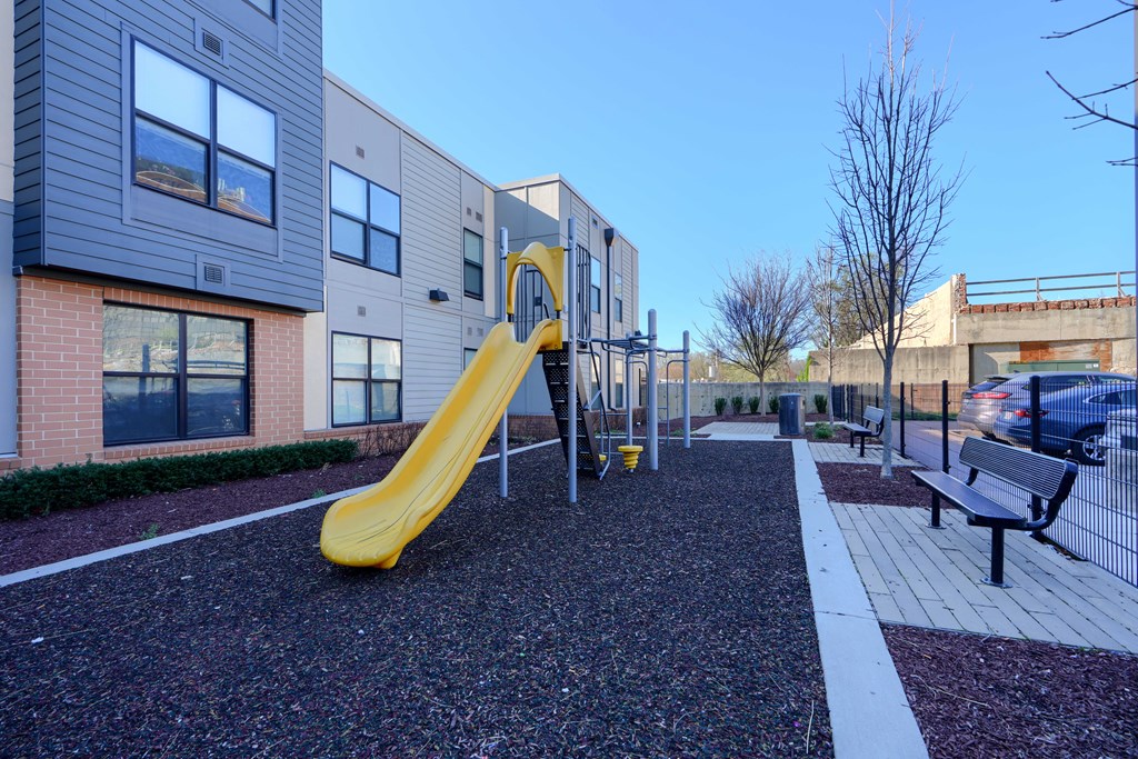 A playground with a yellow slide in front of a building.
