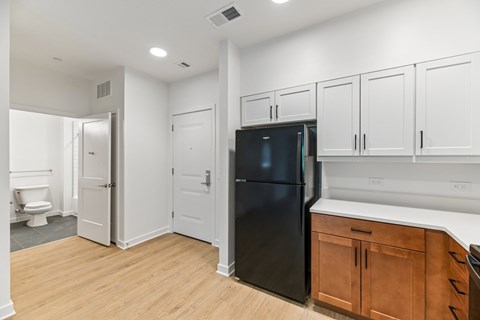 A black refrigerator is in a kitchen with white cabinets and a wooden floor.