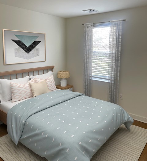 A bed with a blue comforter with white dots is in the foreground of a room with a window and a picture on the wall.