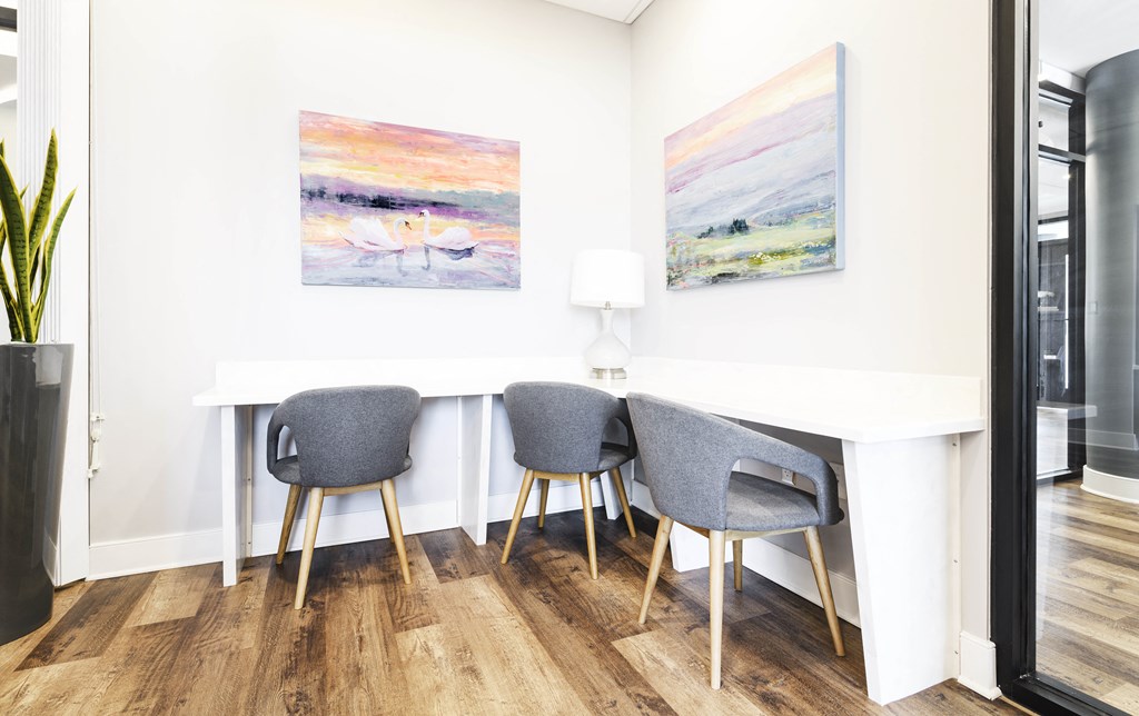 a home office with two paintings on the wall and a white table with three gray chairs