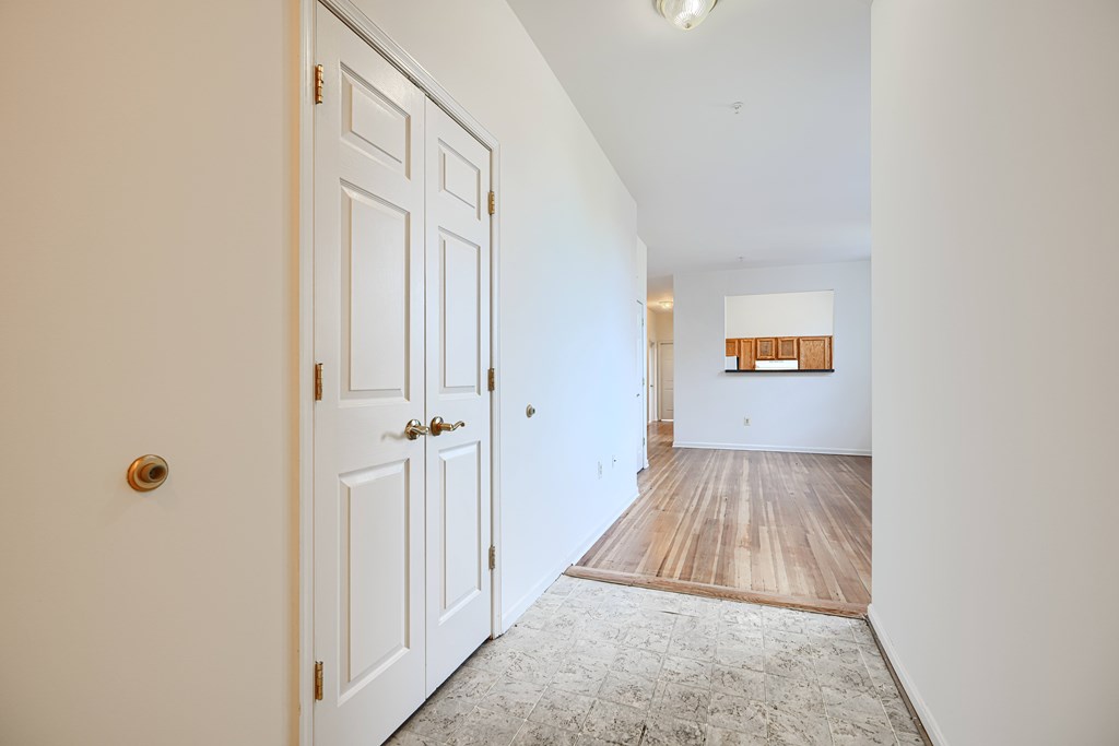 A white door with a gold handle is on the left of a hallway with a wooden floor and a white wall.