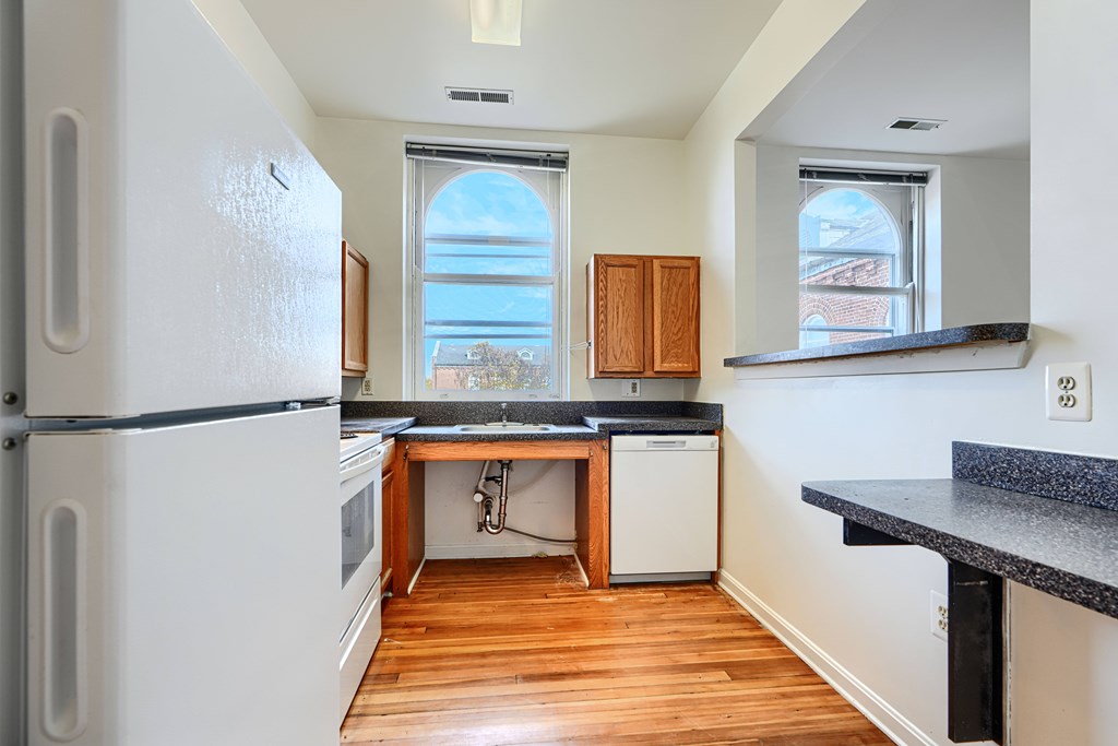 A kitchen with a white fridge and wooden floors.