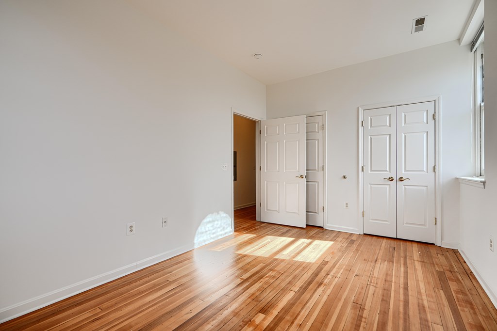 A room with wooden floors and white walls with a door on the left and two closets on the right.