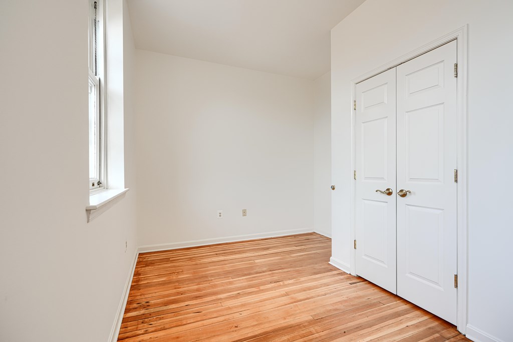 A room with a wooden floor and white walls with a door and a window.