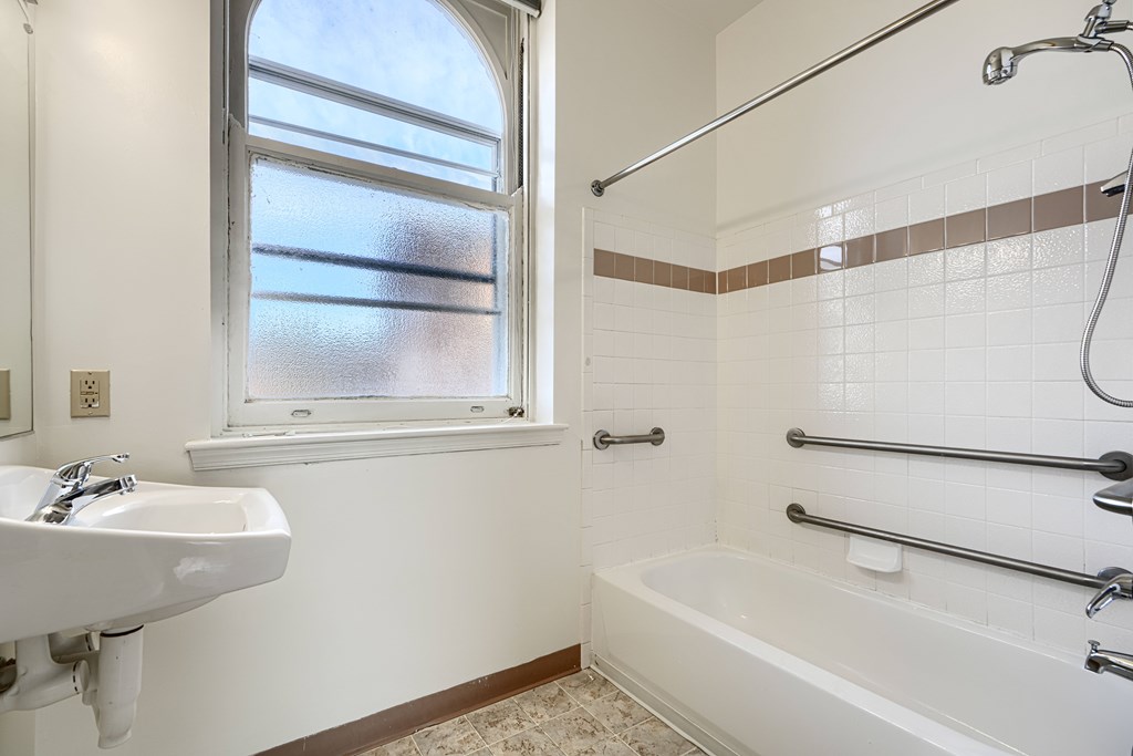 A white sink is on the left side of a bathroom with a window and a bathtub.