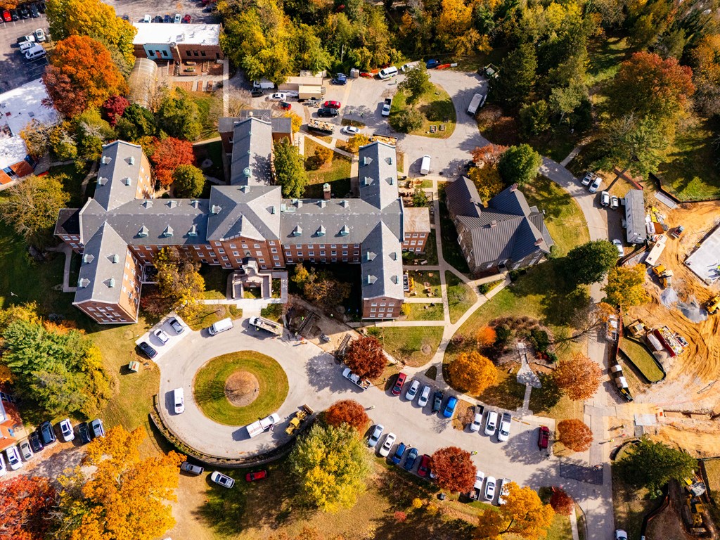 An aerial view of a campus with a large building in the center and a parking lot with cars.