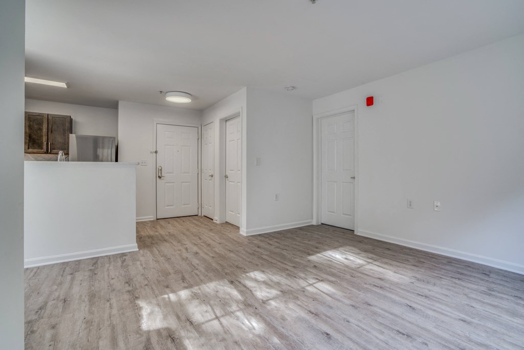 the living room and kitchen of an apartment with white walls and wood flooring