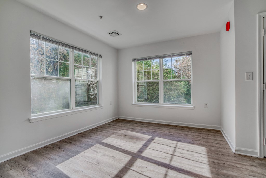 an empty living room with two windows and wood floors