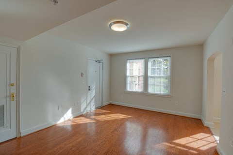 a living room with white walls and wood floors and a window