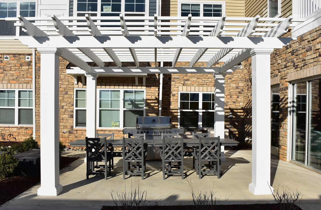 a patio grilling area with a table and chairs under a white pergola