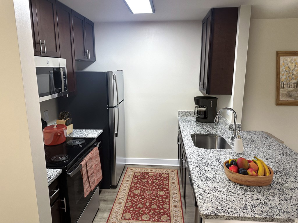 a kitchen with black appliances and granite countertops and a bowl of fruit