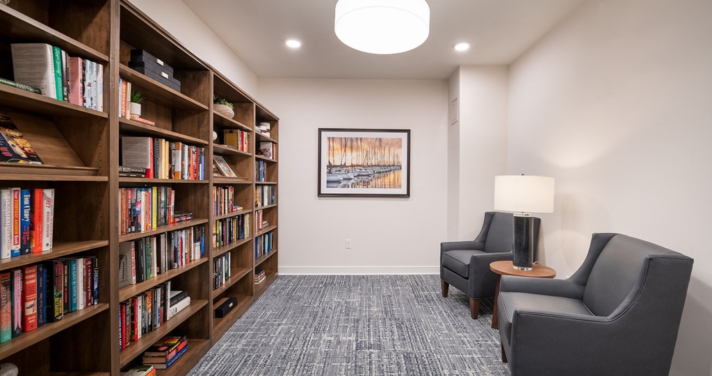 room with chairs and bookshelves and a table with a lamp