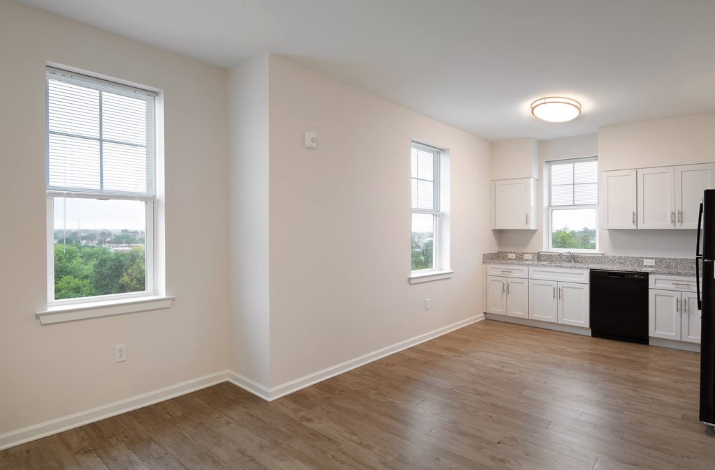an empty kitchen with white cabinets and a wooden floor and a window