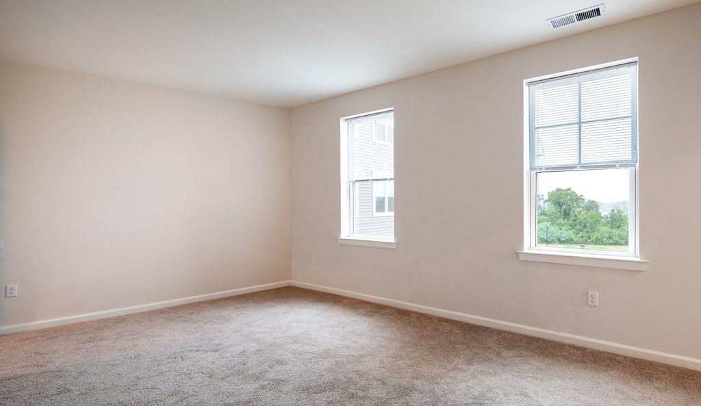 an empty bedroom with two windows and carpeting