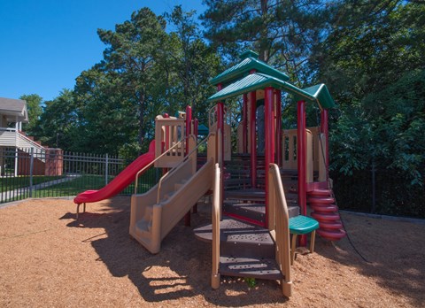 A playground with a red slide and a green roofed structure.