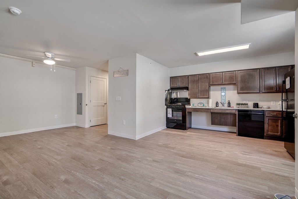 an empty living room and kitchen with wood flooring and black appliances