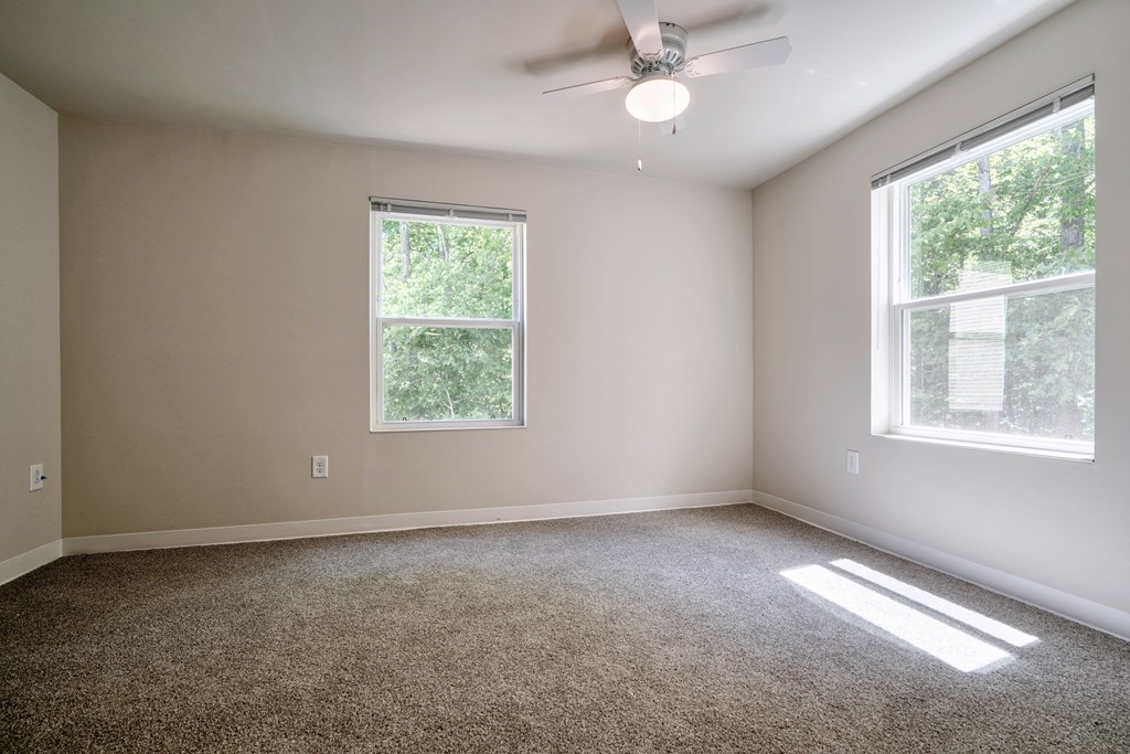 an empty room with two windows and a ceiling fan