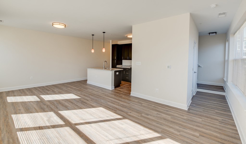 an empty living room and kitchen with wood flooring and white walls