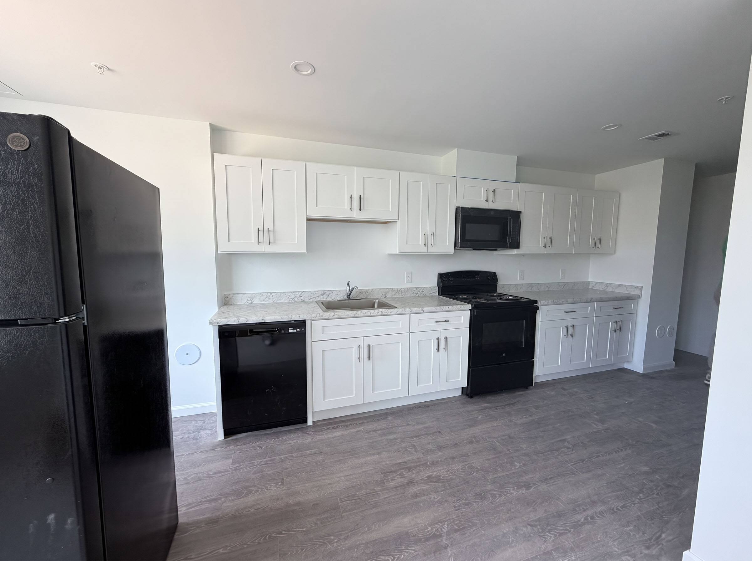 A black refrigerator stands in a kitchen with white cabinets and a marble backsplash.
